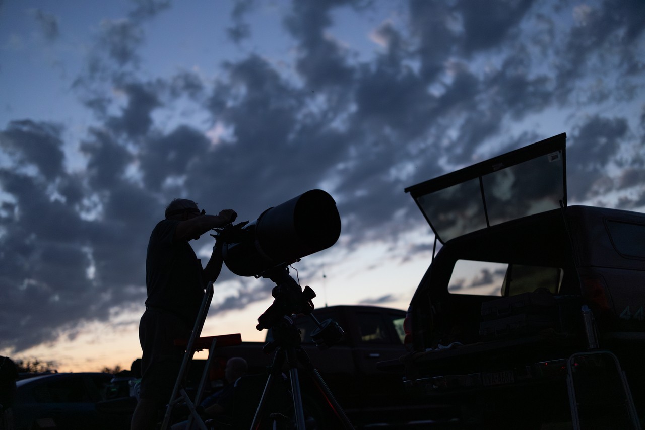 Silhouette of man looking through telescope at dusk