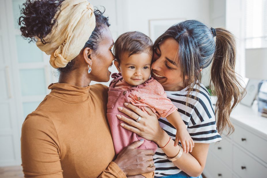 Two smiling women holding a baby in between them.